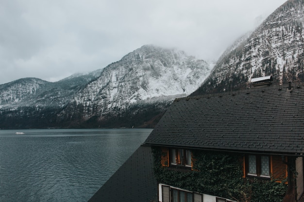 Mooi schot van een huis dichtbij het meer en grijze bergen die overdag met sneeuw worden behandeld