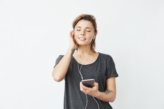 Mooi teder jong meisje glimlachend luisteren muziek in koptelefoon met gesloten ogen.