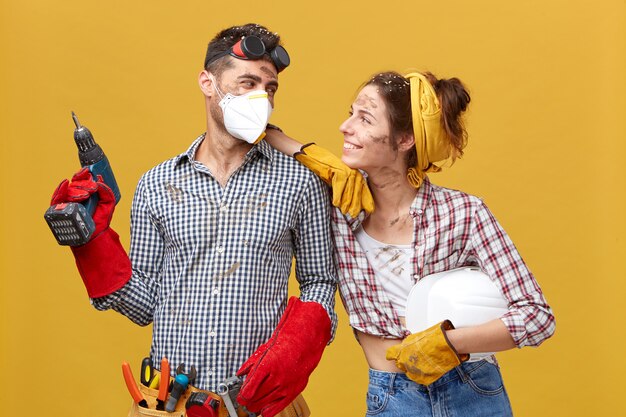 Mooi verliefd stel doet samen bouwwerken. Jonge vrouw die een geruit overhemd en spijkerbroek draagt die met een glimlach naar haar echtgenoot kijkt die een getalenteerde mounter is. Goede relaties en handig werk