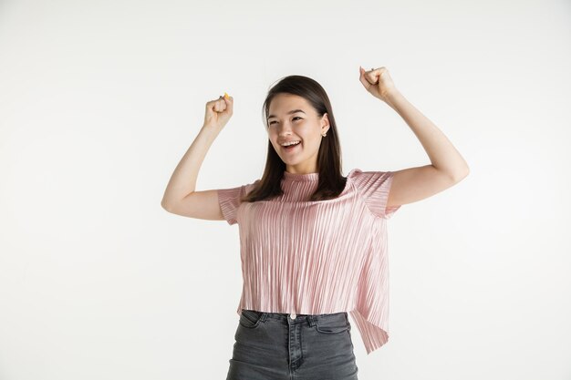 Mooi vrouwelijk half-lengteportret dat op witte studioachtergrond wordt geïsoleerd. Jonge emotionele vrouw in vrijetijdskleding. Menselijke emoties, gezichtsuitdrukking concept. Vieren als winnaar, ziet er gelukkig uit.