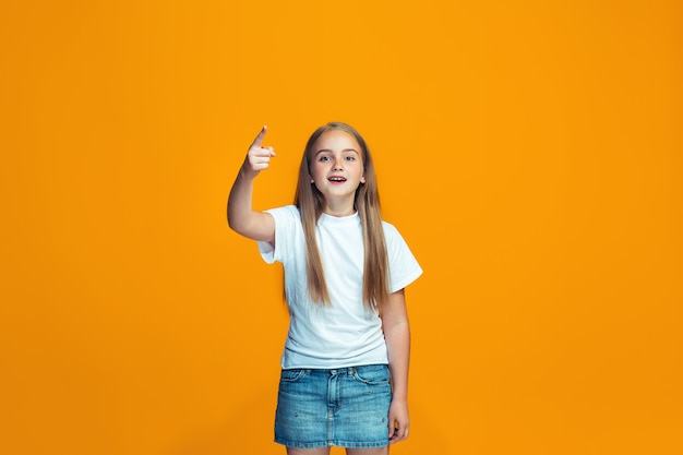 Mooi vrouwelijk half-length portret op oranje studio backgroud. Het jonge emotionele tienermeisje