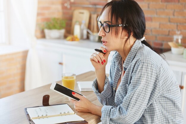 Mooi vrouwelijk model met donkere paardenstaart, nonchalant gekleed, maakt gebruik van moderne digitale tablet,