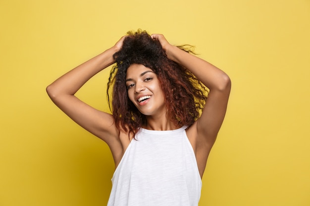 Mooie aantrekkelijke Afro-Amerikaanse vrouwspelen met haar krullend afro haar. Gele studio achtergrond. Ruimte kopiëren.