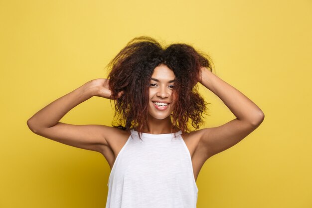 Mooie aantrekkelijke Afro-Amerikaanse vrouwspelen met haar krullend afro haar. Gele studio achtergrond. Ruimte kopiëren.