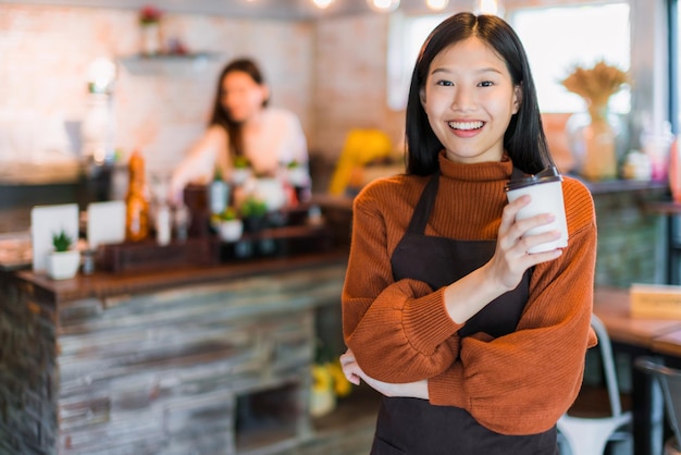 Mooie aantrekkelijke aziatische café-eigenaar glimlach met geluk en blij met koffiekopje schort café-achtergrond