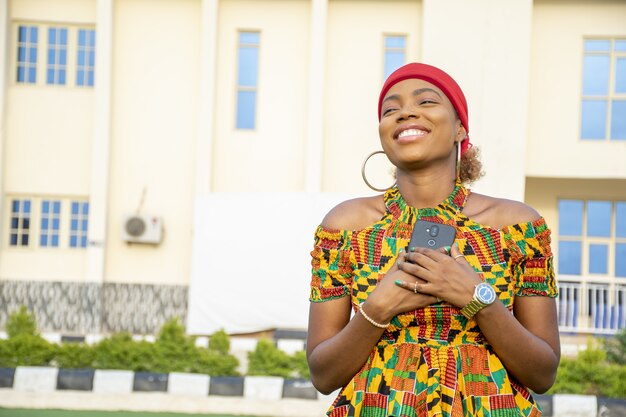 Mooie Afrikaanse dame die haar telefoon vol vreugde tegen haar borst houdt