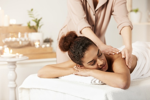 Mooie Afrikaanse vrouw die genietend van massage met gesloten ogen in kuuroordsalon glimlachen.