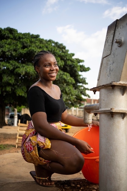 Gratis foto mooie afrikaanse vrouw die wat water in een emmer doet