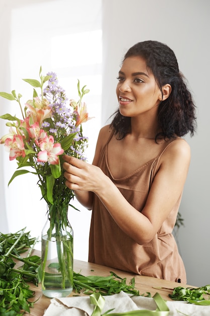 Mooie Afrikaanse vrouwelijke bloemist die makend boeket van bloemen glimlachen.