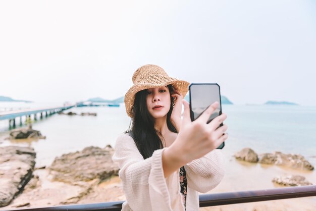 Mooie aziatische vrouw die een zwempak draagt, maakt een selfie op het strand in de zomer op vakantie