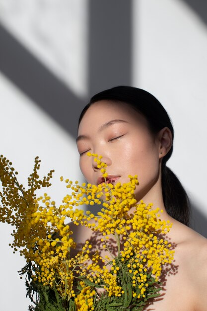 Mooie aziatische vrouw die zich voordeed met gele bloemen met een perfecte huid