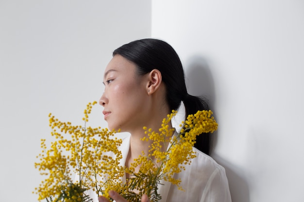 Gratis foto mooie aziatische vrouw die zich voordeed met gele bloemen met een perfecte huid