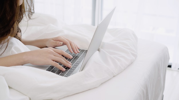 Mooie Aziatische vrouwen speelcomputer of laptop terwijl het liggen op het bed in haar slaapkamer.