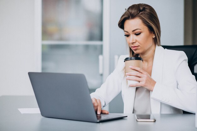 Mooie bedrijfsvrouw die aan computer in bureau werkt en koffie drinkt