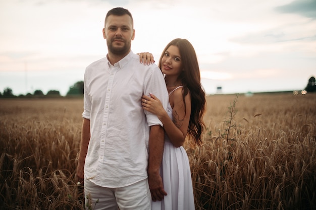 Mooie blanke vrouw met lang donker golvend haar in witte jurk knuffelt met mooie man in wit t-shirt en korte broek