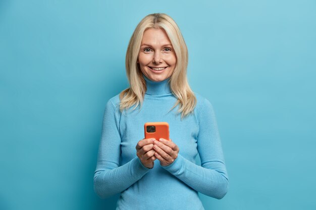 Mooie blonde gerimpelde vrouw overboekingen online geld houdt mobiele telefoon