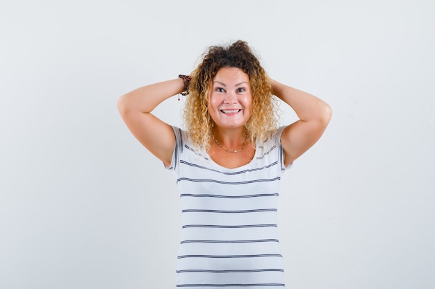 Mooie blonde vrouw die haar handen achter het hoofd houdt in een gestreept t-shirt en er zalig uitziet. vooraanzicht.