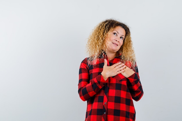 Gratis foto mooie blonde vrouw die haar handen op de borst houdt in een geruit overhemd en er dromerig uitziet, vooraanzicht.