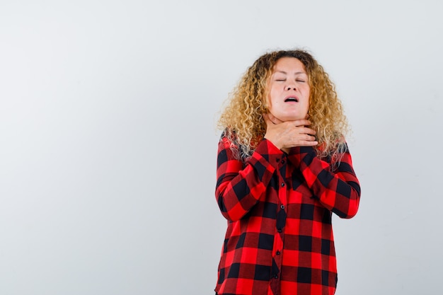 Mooie blonde vrouw die lijdt aan keelpijn in geruit overhemd en er onwel uitziet. vooraanzicht.