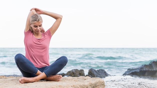 Mooie blonde vrouw die zich uitstrekt op het strand