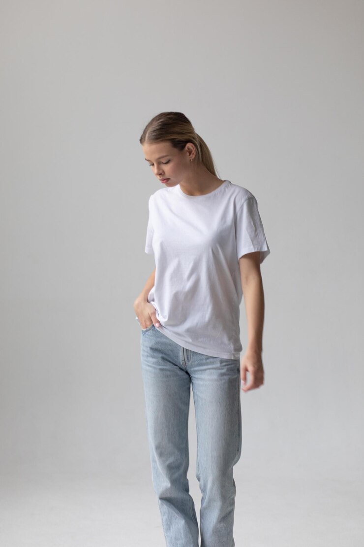 Mooie blonde vrouw in een wit T-shirt en blauwe spijkerbroek die op een witte achtergrond poseert