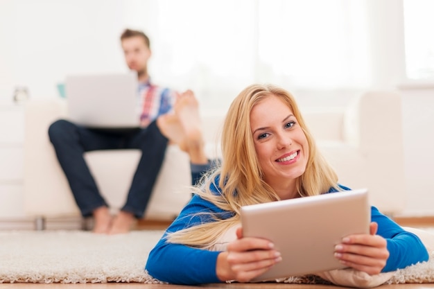 Mooie blonde vrouw met behulp van digitale tablet en ontspannen op capet thuis