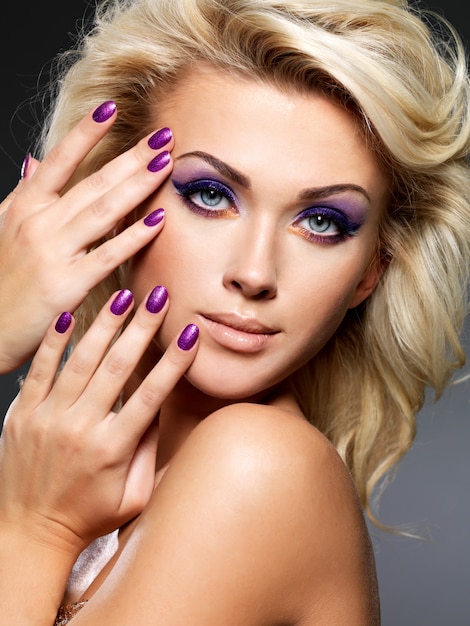 Mooie blonde vrouw met schoonheid paarse manicure en make-up van de ogen