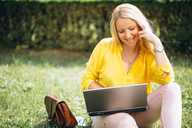 Mooie blonde zitting op gras en het werken aan laptop