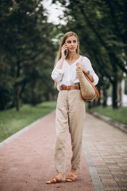 Mooie blondevrouw die telefoon buiten in park met behulp van