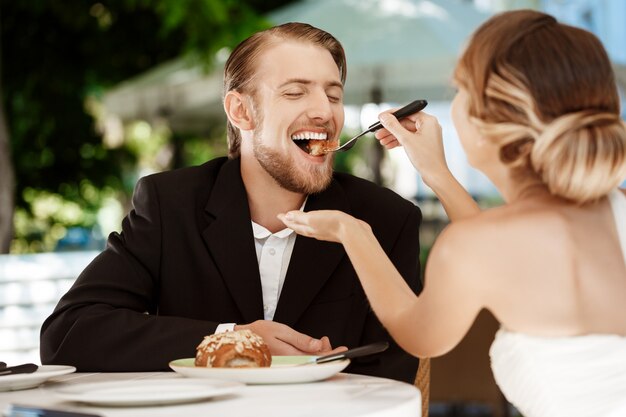 Mooie bruid die haar bruidegom met croissant in koffie voeden.