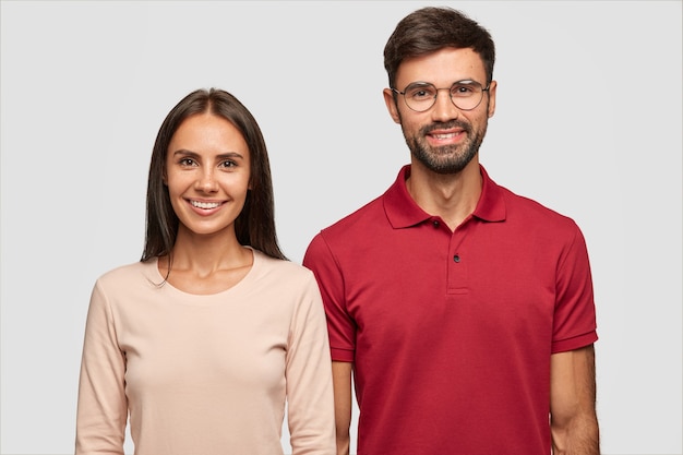 Mooie brunette jonge vrouw met gebruinde huid, brede glimlach, donker lang haar, gekleed in casual swetaer die graag vrije tijd doorbrengt in gezelschap van beste vriend, positief samen glimlachen, binnen staan