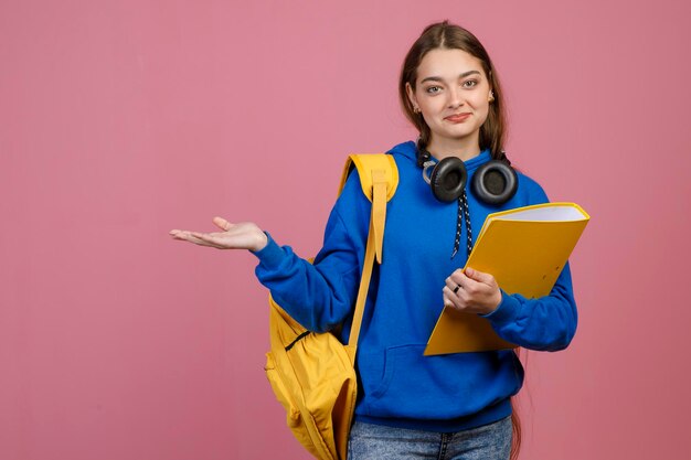 Mooie brunette schoolmeisje staande met gele rugzak en map