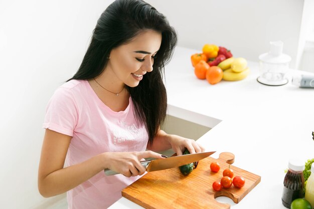 Mooie brunette snijdt groenten op de houten plank in de keuken