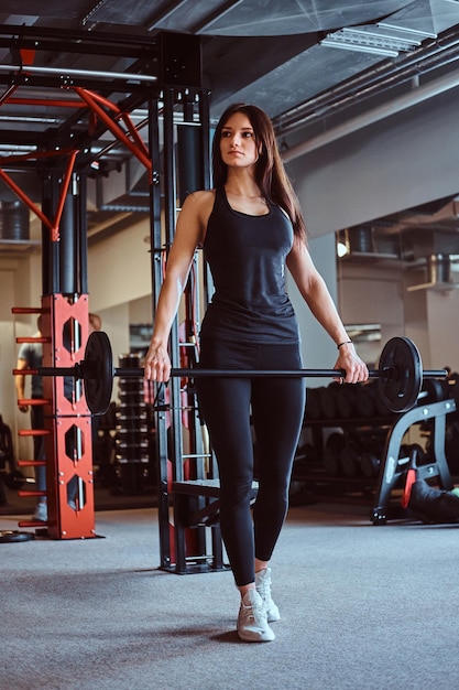 Mooie brunette vrouw in sportkleding houdt een halter vast tijdens het trainen in de fitnessclub of sportschool.