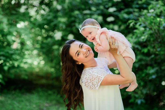 Mooie brunette vrouw in witte jurk staat met haar kleine dochter in de tuin