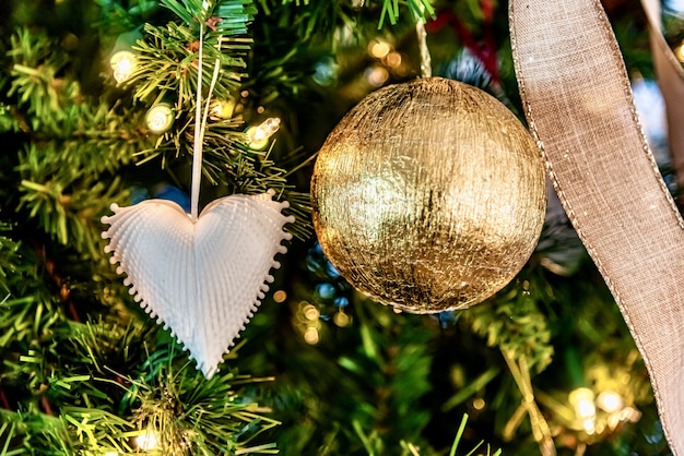 Mooie close-up van een wit hartvormig ornament en een gouden bal op een kerstboom