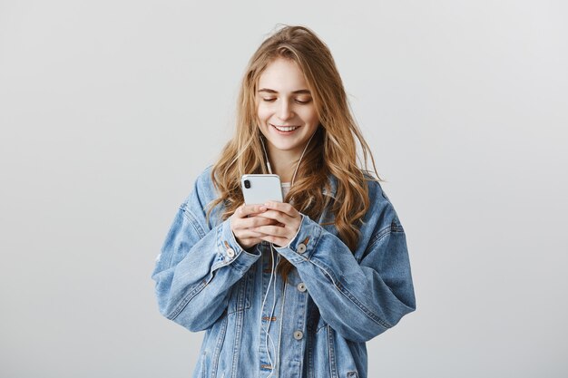 Mooie college meisje texting, messaging en muziek in hoofdtelefoons luisteren