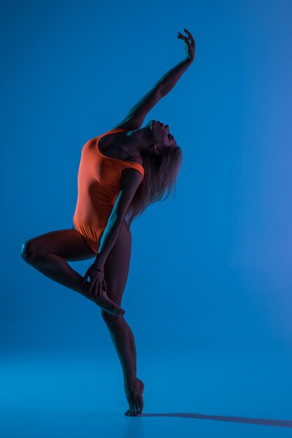 Mooie coole jonge fit gymnast vrouw in blauwe sportkleding jurk uit te werken, art gymnastiek element uitvoeren, springen, split sprong in de lucht doen, dansen