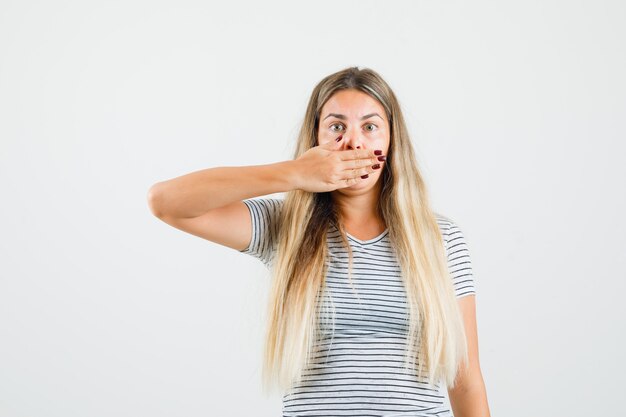 Mooie dame die hand op haar mond in t-shirt houdt en stil kijkt. vooraanzicht.