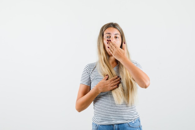 Gratis foto mooie dame die hand op mond en borst in t-shirt houdt en onrustig kijkt. vooraanzicht.