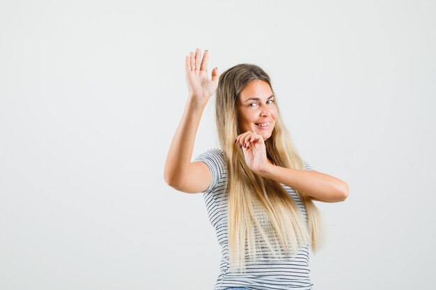 Mooie dame die handen opheft tijdens het dansen in een t-shirt en op zoek geamuseerd, vooraanzicht.