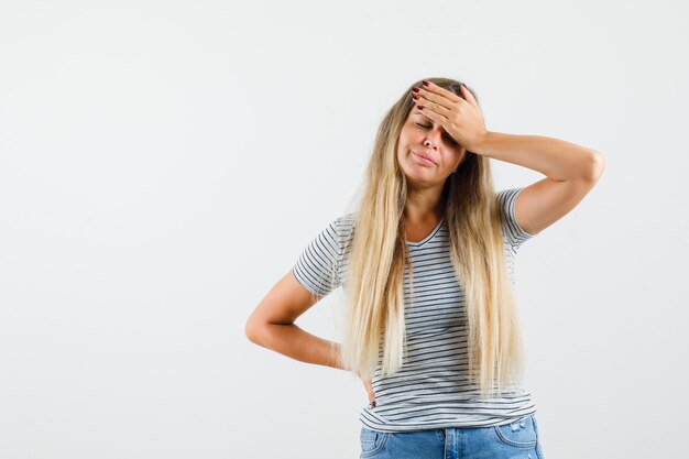 Mooie dame die in t-shirt hand op haar hoofd houdt en uitgeput, vooraanzicht kijkt.