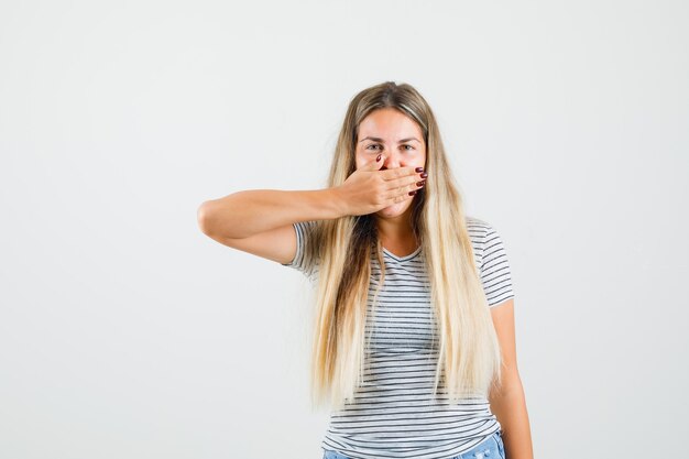 Mooie dame die met hand op mond in t-shirt hoest en moe, vooraanzicht kijkt.