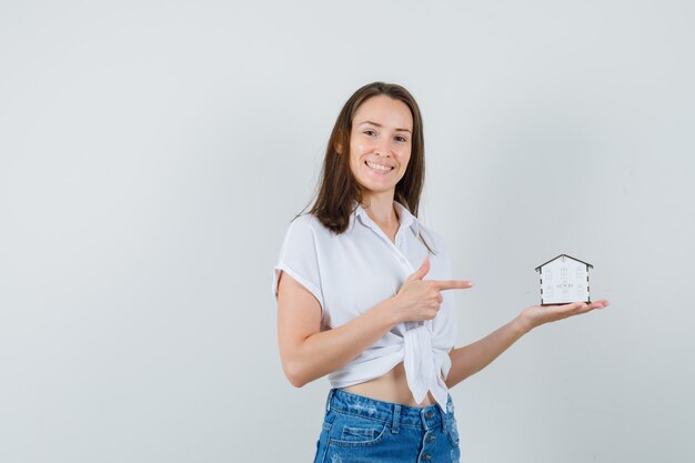 Mooie dame die op modelhuis in witte blouse richt en vrolijk kijkt. vooraanzicht.