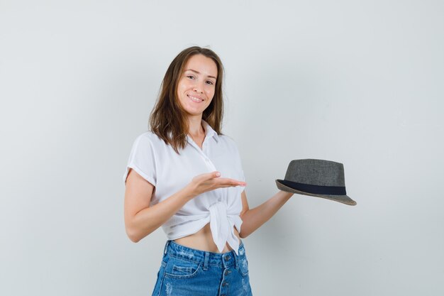 Mooie dame die palm spreidt voor het tonen van haar hoed in witte blouse, hoed.