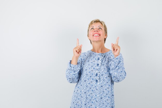 Mooie dame in blouse met patroon die omhoog wijst en gericht, vooraanzicht kijkt.