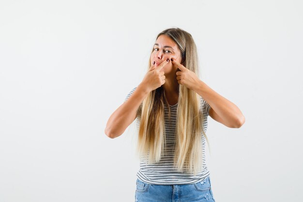 Mooie dame in t-shirt knijpen haar puistjes en op zoek gericht, vooraanzicht.