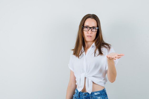 Mooie dame in witte blouse, glazen hand met open palm opheffen en blij op zoek, vooraanzicht.