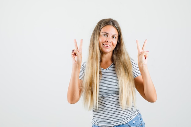 Mooie dame met v-sign met beide handen in t-shirt en op zoek vrolijk, vooraanzicht.