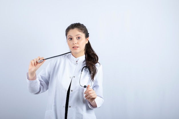 Mooie dokter in witte jas kijkt verbaasd over witte muur.